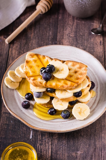 A stack of waffles with banana blueberries and honey on a plate Comfort food Vertical view