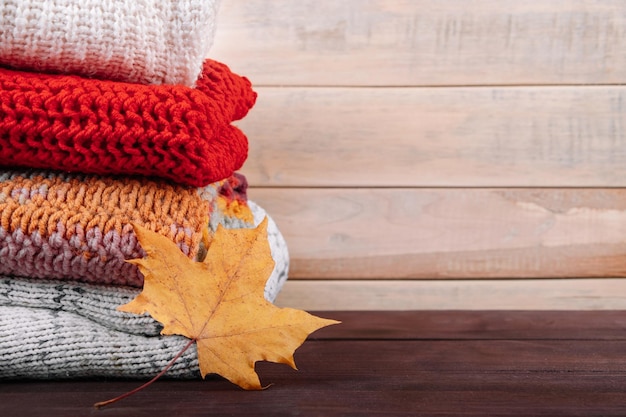 Stack of warm knitted sweaters Autumn concept Woolen jumpers and maple leaf on wooden background