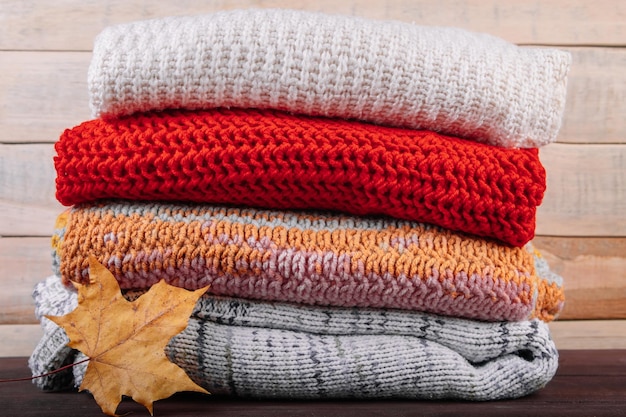 Stack of warm knitted sweaters Autumn concept Woolen jumpers and maple leaf on wooden background