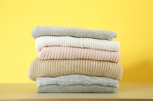 A stack of warm sweaters on the table on a colored background