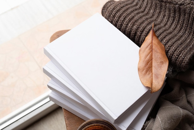 Stack of white blank books with autumn leaves and cup of hot tea on old wooden chair mockup design