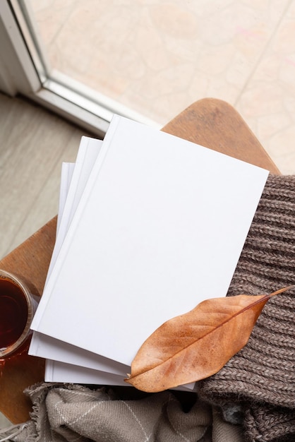 Stack of white blank books with autumn leaves and cup of hot tea on old wooden chair mockup design