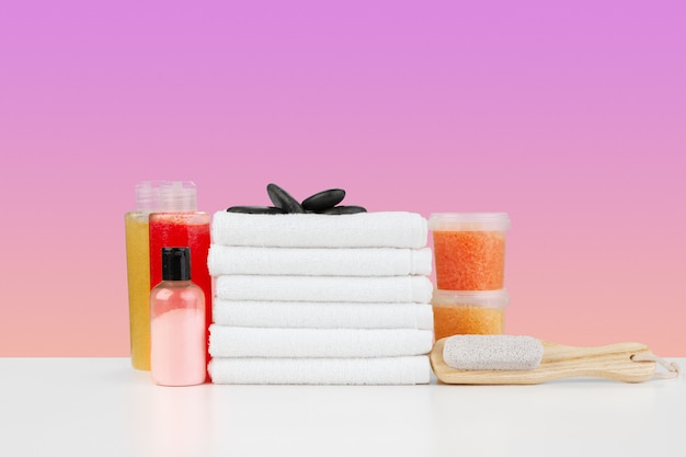 Stack of white towels and bottles of skincare on white table