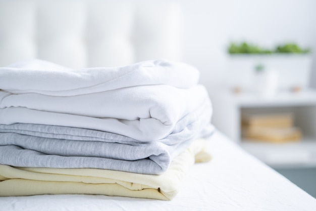 Stack of women colorful sweatshirts, hoodies in pastel colors on white bed. Seasonal shopping, laundry, vacation concept.