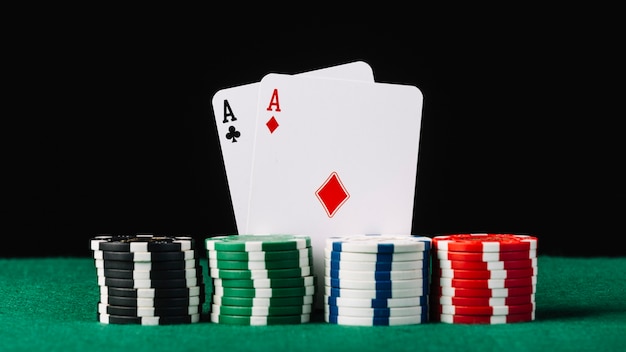 Stacked casino chips in front of two aces on poker table