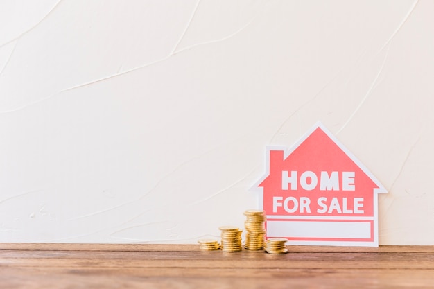 Stacked coins with home for sale icon leaning on wall