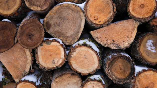 Stacked wooden sawn logs covered with snow and laid out in several rows