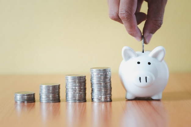 Stacking coins pile and Hand putting coin into white piggy bank for savings with money and planning step up to growing, Saving money for retirement fund and the future plan concept.