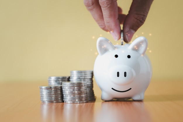 Stacking coins pile and Hand putting coin into white piggy bank for savings with money and planning step up to growing, Saving money for retirement fund and the future plan concept.