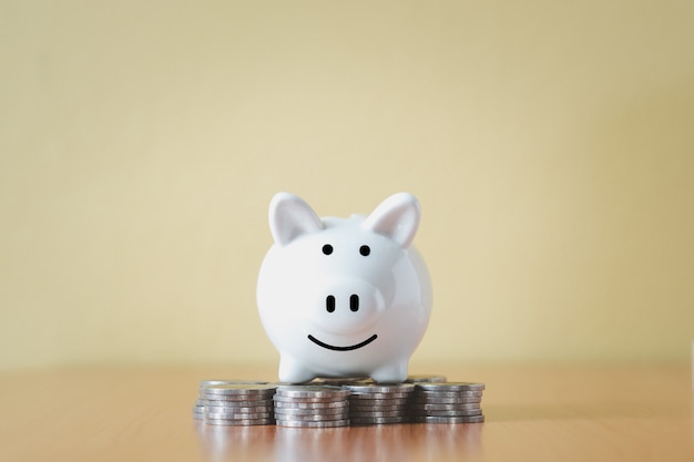 Stacking coins pile and white piggy bank for savings with money and planning step up to growing, Saving money for retirement fund and the future plan concept.