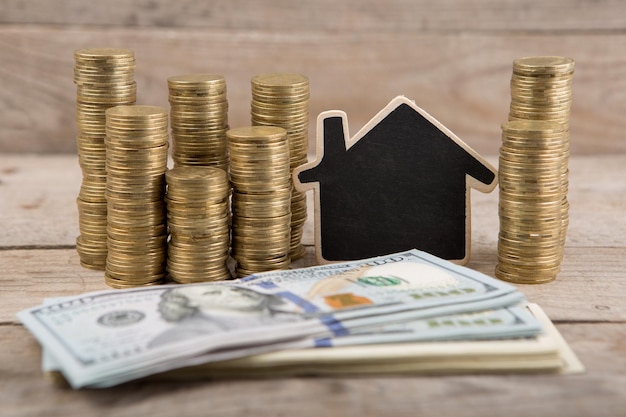 Stacks of coins and dollar bills blank blackboard in the shape of a house