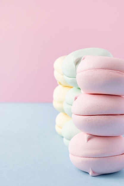 Stacks of colorful marshmallows on pastel pink and blue background closeup