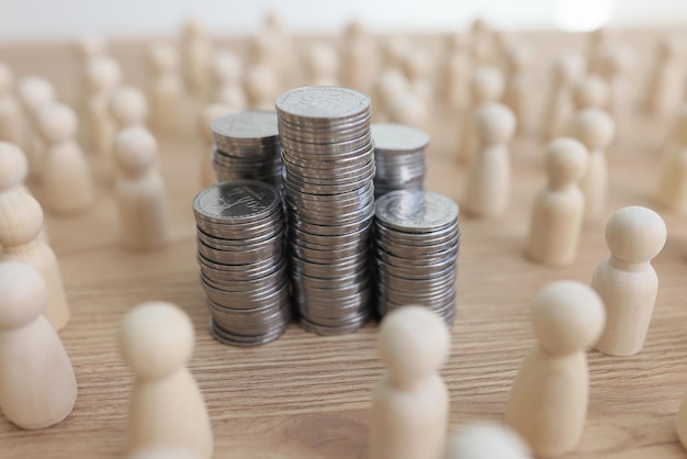 Stacks of silver coins surrounded by white figurines of employees standing on wooden table