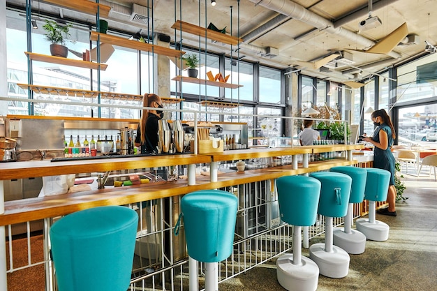 Staff with masks near long counter with bar stools in cafe