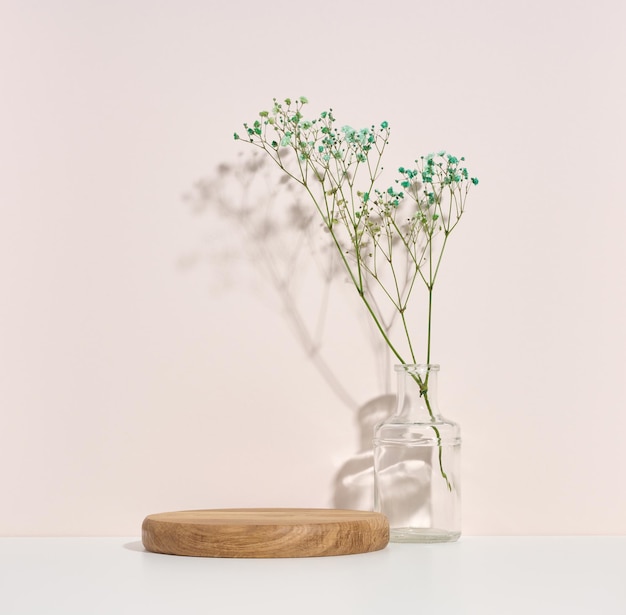 Stage for displaying products cosmetics with a round wooden podium and a glass vase with a bouquet of flowers