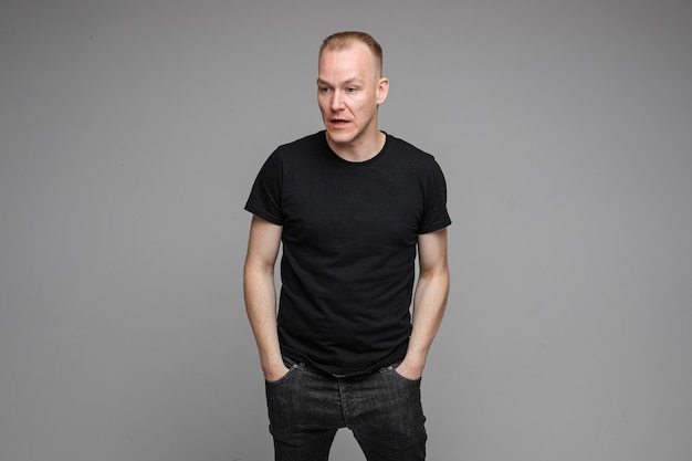 Staged photo of a Caucasian man in black clothes keeping hands in pockets and looking confused