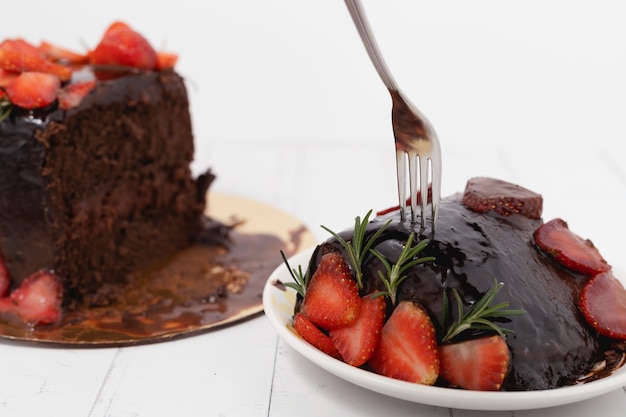 A stainless fork scooping a piece of delicious chocolate cake with strawberries on white background for food and bakery concept