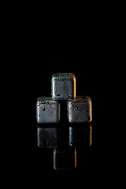 Stainless steel cubes simulating ice for cooling drinks on a black surface with a reflection