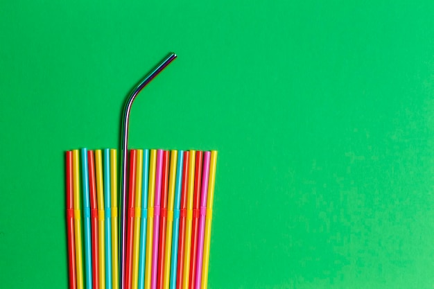 Stainless steel reusable drinking straw with plastic straws on green background