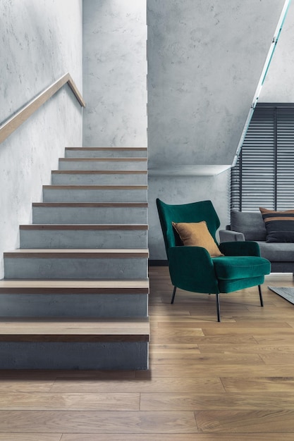 Stairs in modern living room interior Green velvet armchair and minimalist personal accessories Concrete walls Home decor Template