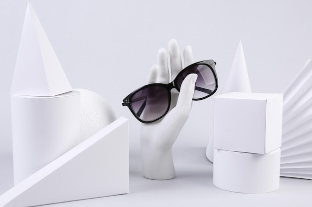 Stand hand holding sunglasses and geometric shapes on white background Concept art Minimalism