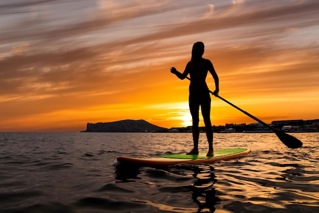 Stand up paddle boarding on a quiet sea with warm summer sunset colors