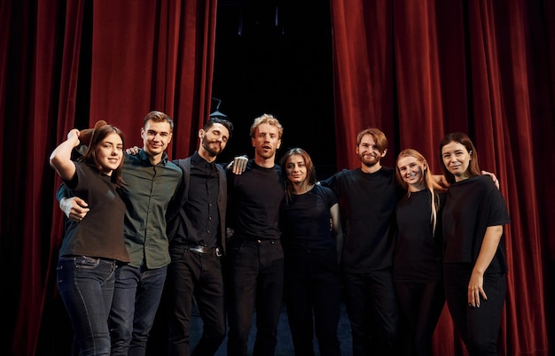 Standing against red curtains Group of actors in dark colored clothes on rehearsal in the theater