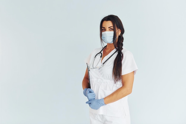 Standing against white background Young female doctor in uniform is indoors