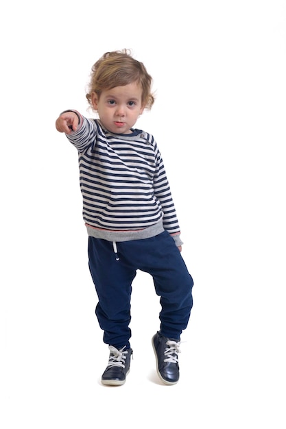 Standing boy looking at camera and pointing finger to the front on white background