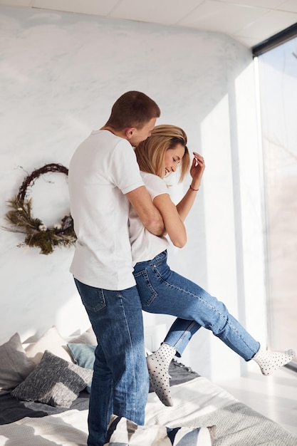 Standing and embracing on bed Young lovely couple together at home spending weekend and holidays together