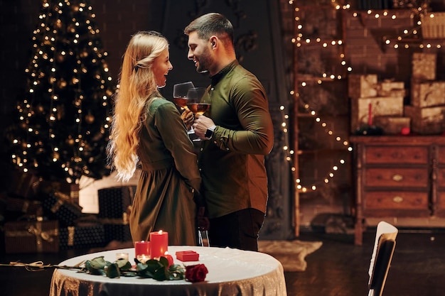 Standing and holding big glasses with wine Young lovely couple have romantic dinner indoors together