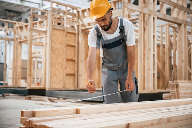 Standing marking plank by pencil Industrial worker in wooden warehouse