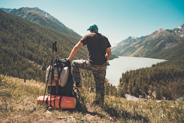 Standing sporty man with backpack on the mountain peak and beautiful mountains atbright sunny day Landscape with man rocks with snowy peaks glacier clouds in altay Travel Trekking Vintage