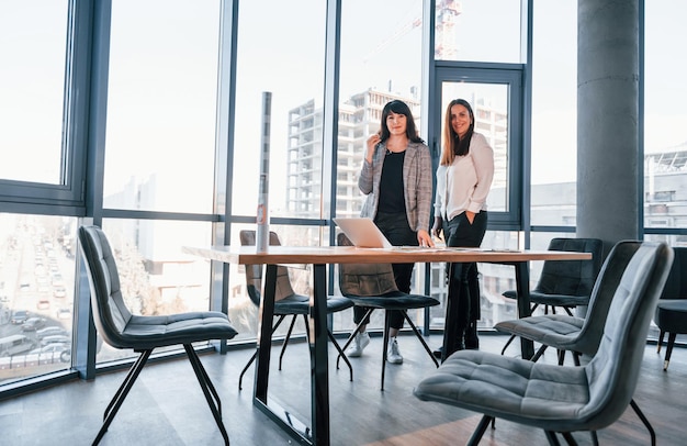 Standing and talking Two women in formal clothes is indoors in the modern office works together