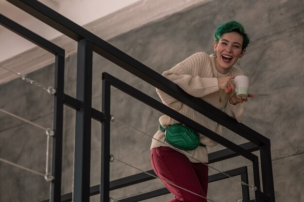 Standing upstairs. Green-haired woman laughing while talking to her family standing upstairs