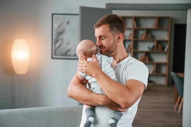 Photo standing with baby in hands father with toddler is at home taking care of his son