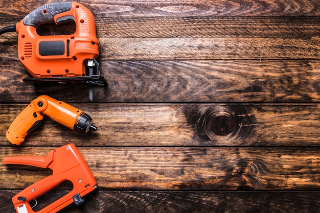 Staple gun, cordless drill and electric jigsaw on wooden surface