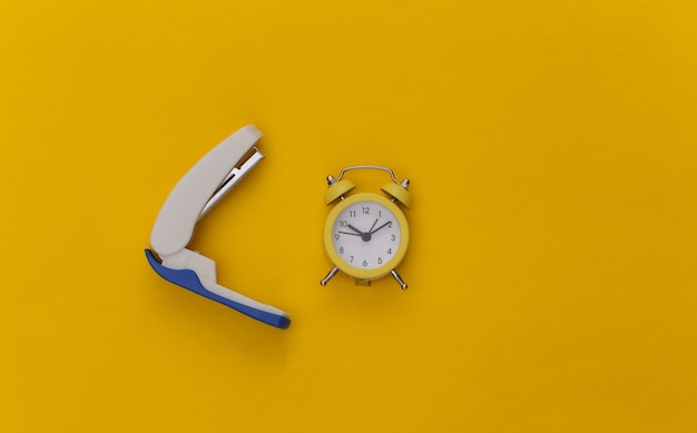 Stapler and alarm clock on a yellow background. Office supplies.