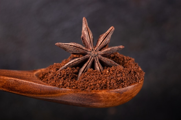 Star anise in a wooden spoon with ground coffee on a dark background