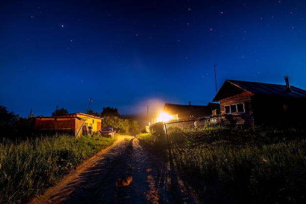 Starry night sky over village house in summer Wooden house with one bulb light over entrance Russia