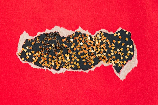 Stars confetti on black background under torn red paper. Christmas holidays concept.