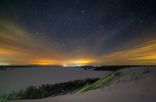 Stars of the night sky are hidden by clouds. Snowy winter landscape at dusk. City in the valley.