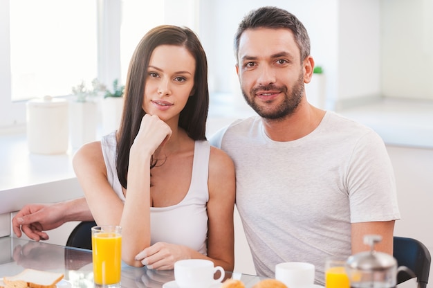 Starting new day together. Beautiful young couple bonding to each other while sitting in the kitchen together and having breakfast