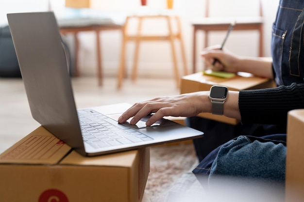 Startup small business owner writing address on cardboard box at workplace Freelance Asian woman small business entrepreneur SME working with box at home