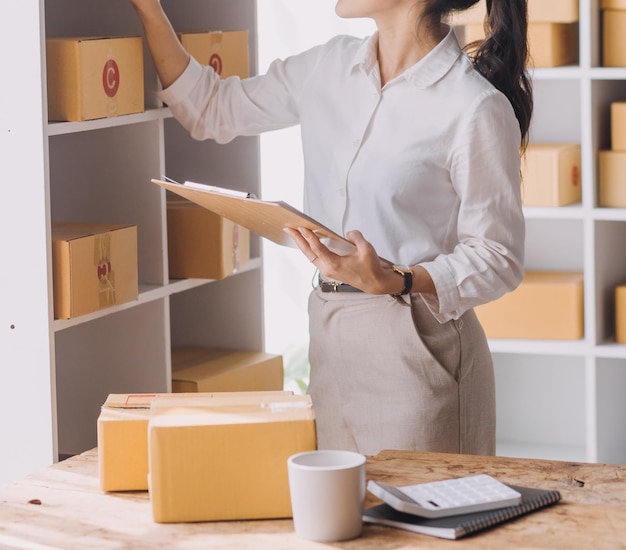 Startup SME small business entrepreneur of freelance Asian woman wearing apron using laptop and box to receive and review orders online to prepare to pack sell to customers online sme business ideas