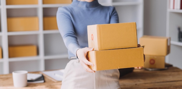 Startup SME small business entrepreneur of freelance Asian woman wearing apron using laptop and box to receive and review orders online to prepare to pack sell to customers online sme business ideas