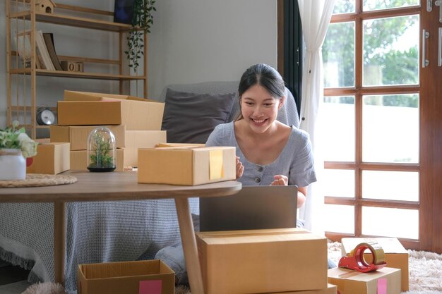 Startup SME small business entrepreneur SME or freelance Asian woman using a laptop with box Young success Asian woman with her hand lift up online marketing packaging box and delivery SME concept