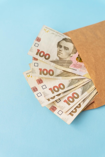 A stash of money in 100hryvnia banknotes coming out of an envelope on a blue background The concept of salary bribe credit debt profit