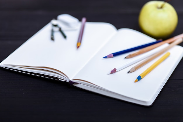 Stationeries and a green apple are on the black table