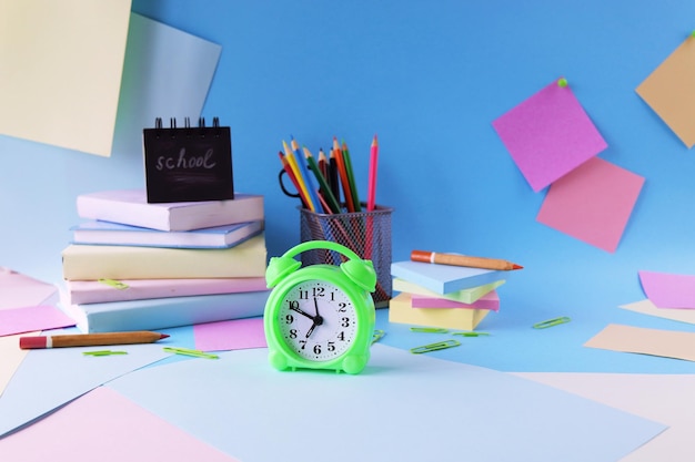 Stationery, alarm clock, books on a background of pastel colors of multi-colored paper